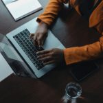 Top down view of a person in business clothing, typing on a laptop on a desk supporting an article on operational costs